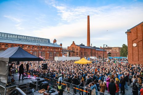 A crowd gathered for an outdoor concert among the brick buildings of Vallilan makasiinit